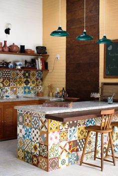 a kitchen with colorful tiles on the counter and wooden chairs in front of it, next to a chalkboard