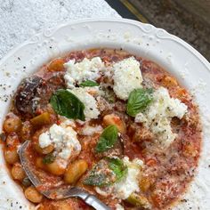 a white plate topped with pasta covered in sauce and cheese next to a silver spoon