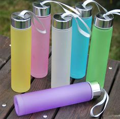 four different colored water bottles sitting next to each other on a wooden table with white ribbon