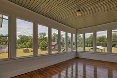 an empty room with wood floors and large windows on each side of the room, looking out onto a grassy field