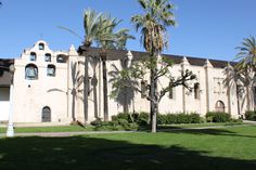 palm trees line the lawn in front of an old building with arched windows and balconies