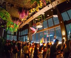 a group of people standing around in a room with lots of windows and plants hanging from the ceiling