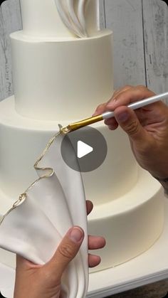 a person is cutting into a white wedding cake