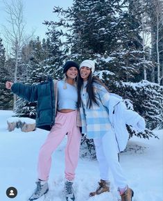 two women are standing in the snow with their arms around each other and one is pointing