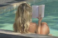 a woman sitting in a pool reading a book with her legs crossed and back to the camera