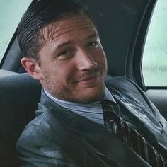 a man sitting in the back seat of a car wearing a suit and tie, smiling