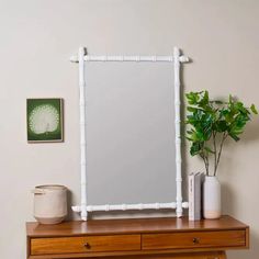 a white mirror sitting on top of a wooden dresser next to a potted plant