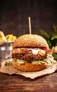 a hamburger with bacon, cheese and lettuce on a wooden table next to fries