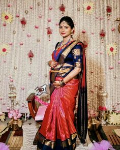 a woman in a red and blue sari standing next to a wall with flowers