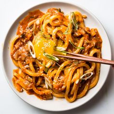 a white plate topped with noodles and meat covered in sauce next to a wooden spoon