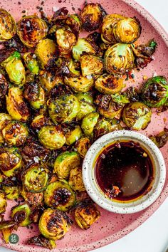 brussel sprouts on a pink plate with a small bowl of dipping sauce