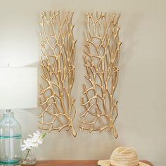 two wall sculptures made out of branches on a table next to a hat and lamp