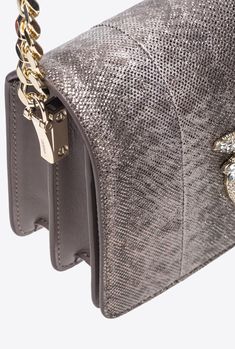 Crossbody Mini Love Bag Click in karung reptile leather with glittery metallic effect. The magnetic button concealed beneath the flap is accompanied by the iconic Love Birds Diamond Cut buckle enhanced by pavé rhinestone detailing. Inside, it features contrasting fabric lining, a leather slip pocket and a zipped divider pocket. The metal chain strap comes with an adjustable leather shoulder pad for greater comfort. The accessory is part of the Limited Edition special capsule collection which com Luxury Silver Shoulder Bag With Gold-tone Hardware, Luxury Metallic Clutch Bag, Luxury Metallic Shoulder Bag With Palladium Hardware, Luxury Metallic Clutch Shoulder Bag, Luxury Silver Shoulder Bag With Magnetic Closure, Luxury Metallic Shoulder Bag For Evening, Luxury Textured Leather Party Bag, Luxury Leather Shoulder Bag With Textured Finish, Luxury Metallic Bags With Gold-tone Hardware