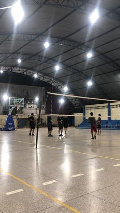 some people are playing volleyball in an indoor court with lights on the ceiling and floor