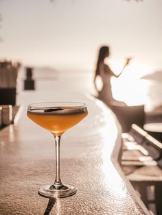 a drink sitting on top of a wooden table next to a woman in the background