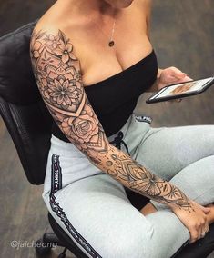 a woman with tattoos sitting on a chair holding a cell phone and looking at the camera