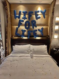 a bed with white sheets and blue letters on the wall above it that says wife for lifey