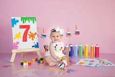 a baby sitting on the floor in front of an easel with paint and crayons