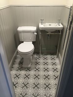 a white toilet sitting next to a sink in a bathroom on top of a tiled floor