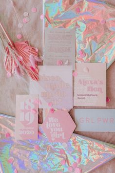 pink and silver wedding stationery with confetti on the table next to it