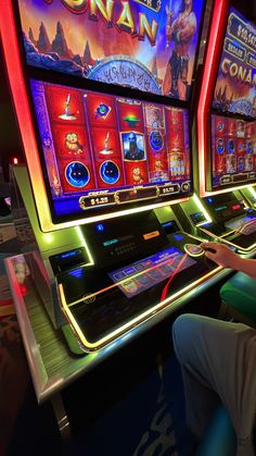 two people playing slot machines in a casino room with neon lights on the front and sides