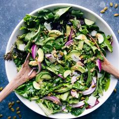 a white bowl filled with greens, onions and cucumber on top of a blue table