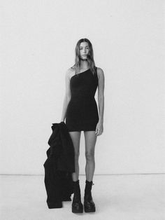 a black and white photo of a woman standing in front of a wall holding a bag