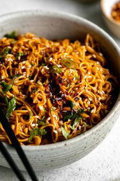 a white bowl filled with noodles and vegetables next to chopsticks on a table