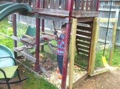 a little boy standing in front of a chicken coop with a slide on the other side