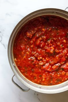 a large pot filled with red sauce and garnished with basil on the side