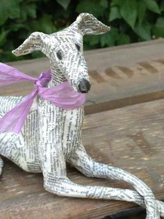 a dog made out of newspaper sitting on top of a wooden bench with a ribbon around it's neck