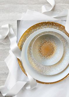 two white and gold plates on top of each other next to some white paper streamers