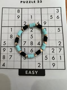 a blue and black beaded bracelet sitting on top of a sud puzzle board with numbers