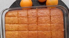 an orange cake in a plastic container next to some oranges