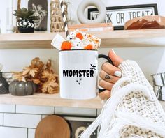 a person holding a coffee mug with marshmallows in it and candy on top