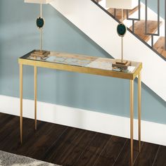 a table with two lamps on it in front of a stair case and blue wall