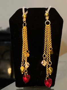 two pairs of earrings with dangling chains and heart shaped beads on top of a black stand