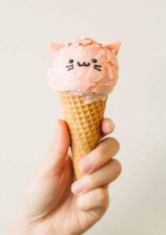 a hand holding an ice cream cone with a cat face on it