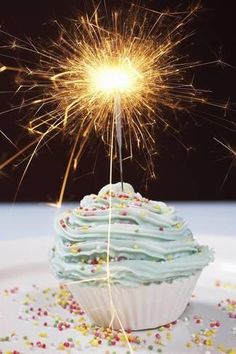 a cupcake with blue frosting and sprinkles on it is being lit by a sparkler