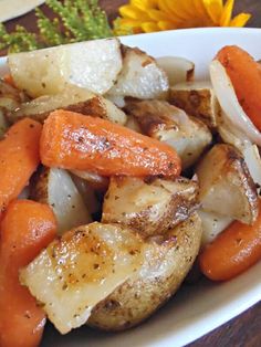 a white plate topped with potatoes and carrots on top of a table next to a yellow flower