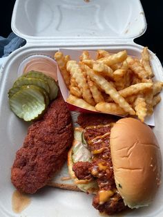 a take out container with a chicken sandwich, fries and pickle on the side