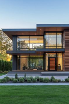 a modern house with large windows and lots of grass in the front yard at dusk