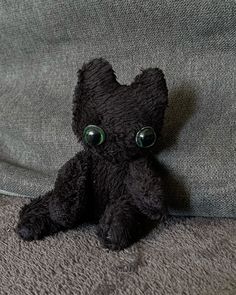 a black teddy bear with green eyes sitting on a gray couch cushion, looking at the camera