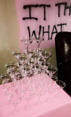 a table topped with lots of wine glasses on top of a pink table cloth next to a black chair