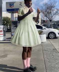 a woman in a green dress and pink socks is standing on the sidewalk with her hand up