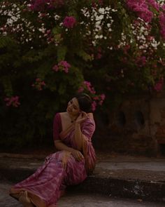 a woman sitting on the steps talking on her cell phone with flowers in the background