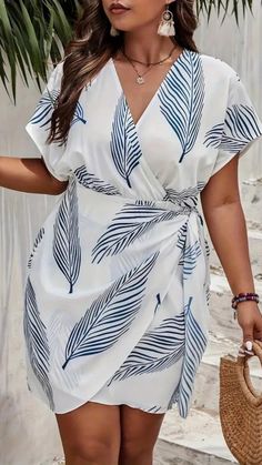 a woman wearing a white dress with blue leaves on it and holding a straw bag