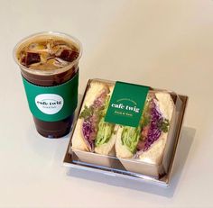 a cup of coffee next to a sandwich in a take out box and a drink