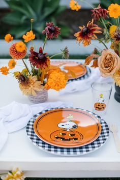 an orange and black place setting with flowers in vases on the table, along with two plates