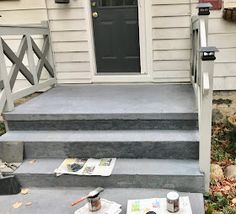 the front steps of a house with paint cans and brushes on them, next to an open door